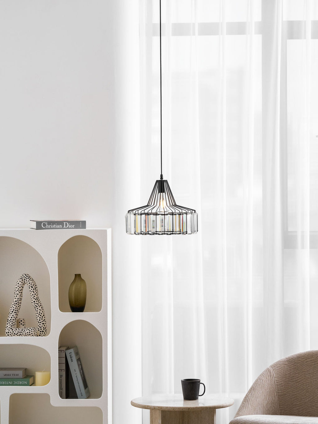 Small black crystal drum pendant from Clérachic in a bright room, with an arched white shelf and a table with a cup beneath.
