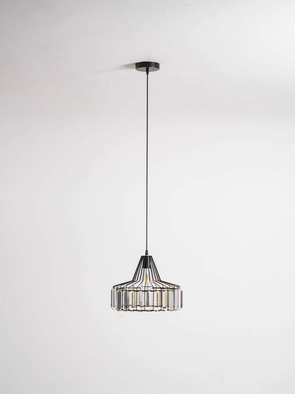 Black crystal drum pendant from Clérachic on a black ceiling plate and long cable, hanging against a pale grey backdrop.