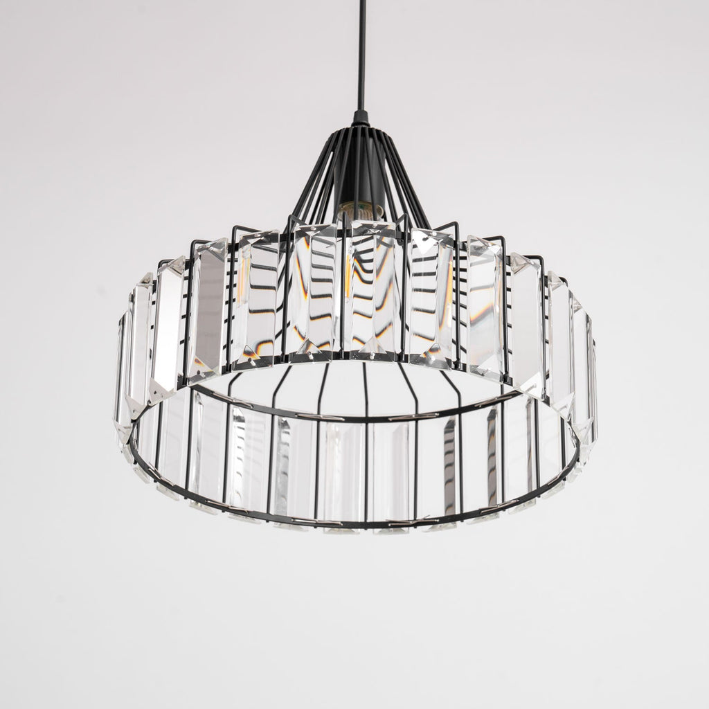 View from below of the black frame and clear prisms of this Clérachic crystal drum pendant, with its bulb visible inside.