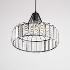 View from below of the black frame and clear prisms of this Clérachic crystal drum pendant, with its bulb visible inside.