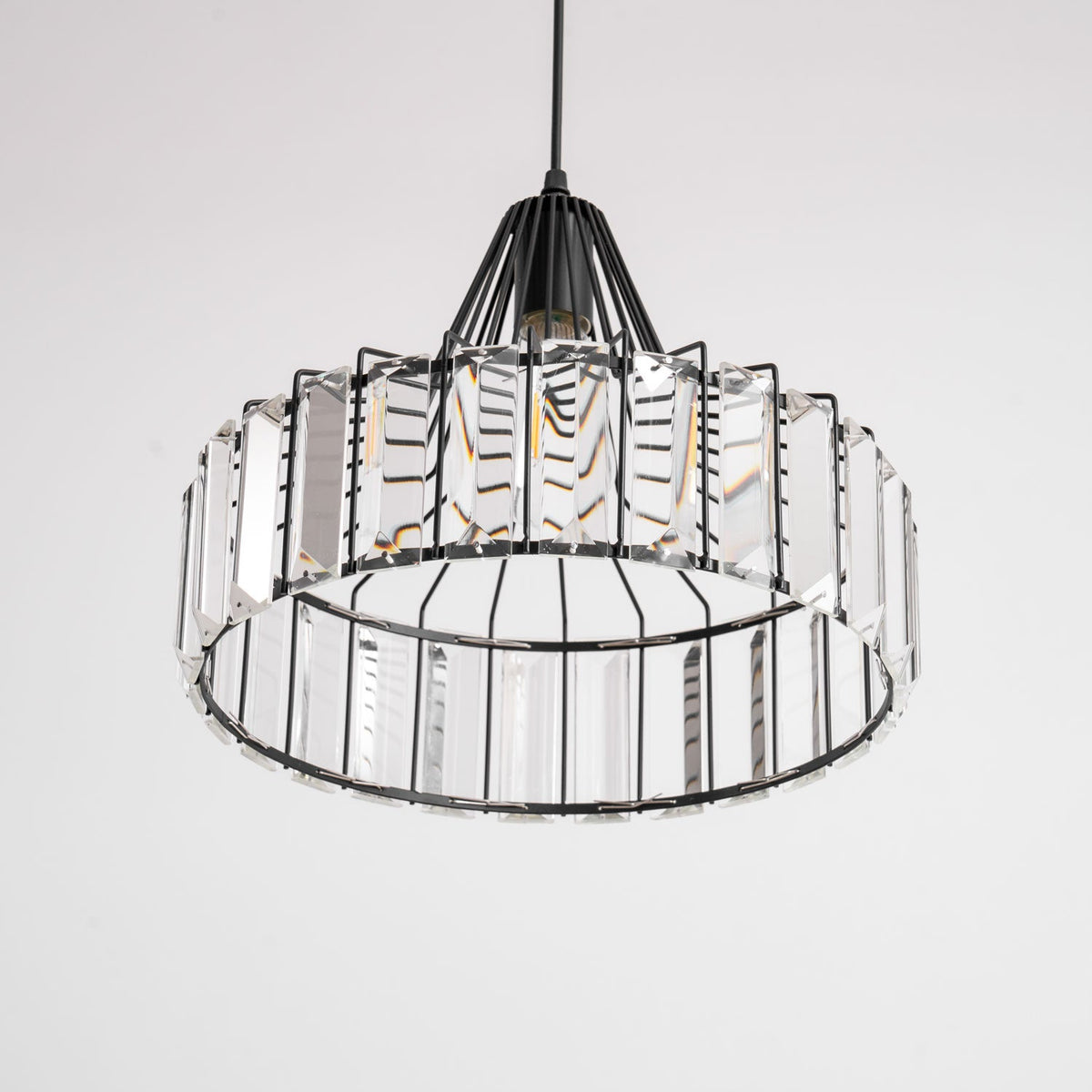 View from below of the black frame and clear prisms of this Clérachic crystal drum pendant, with its bulb visible inside.