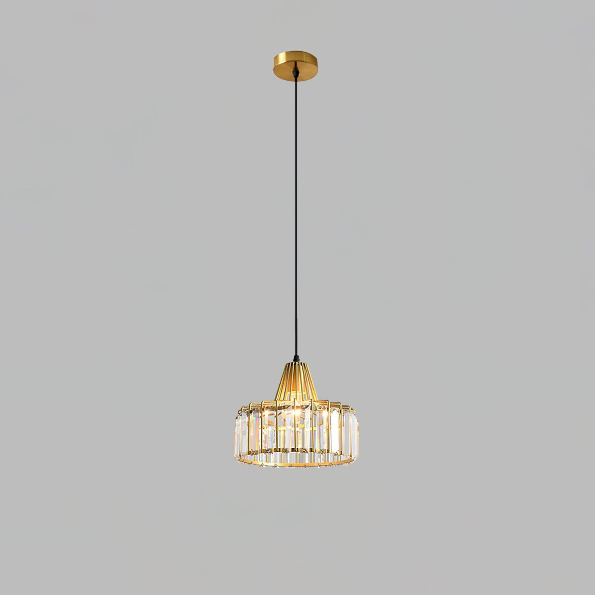 Gold crystal drum pendant from Clérachic on a gold ceiling plate and long cable, against a flat grey backdrop.