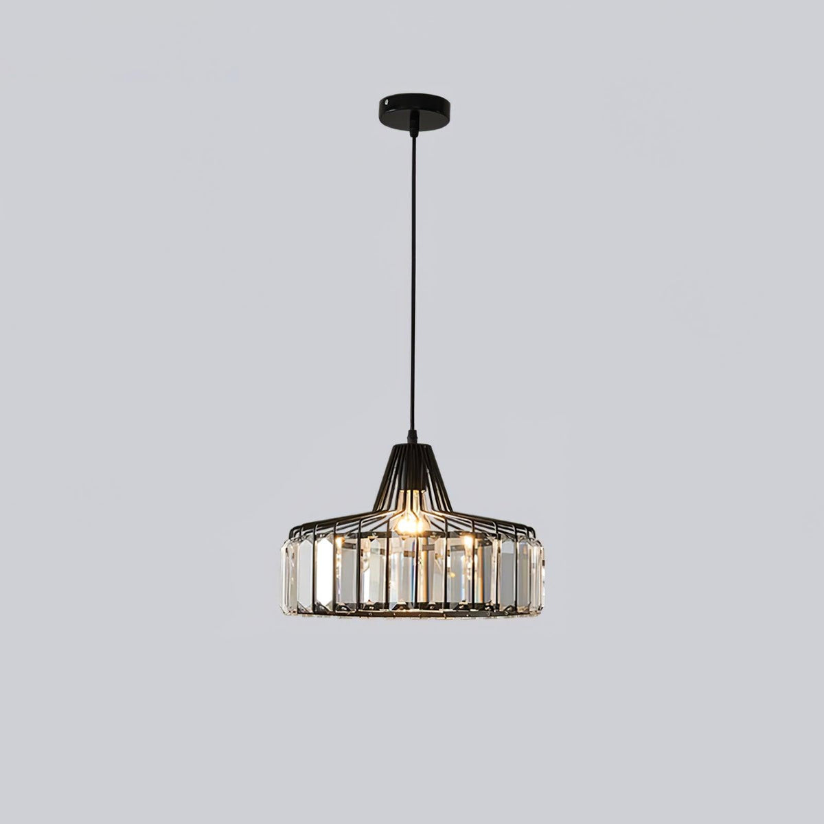 Black crystal drum pendant from Clérachic on a black ceiling plate, lit, hanging on a long cable against a light grey backdrop.