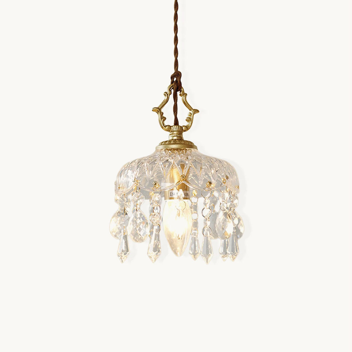 A Clérachic pendant light on a plain white backdrop, a ribbed glass dome with crystal drops and a gold hanger on a twisted brown cord.