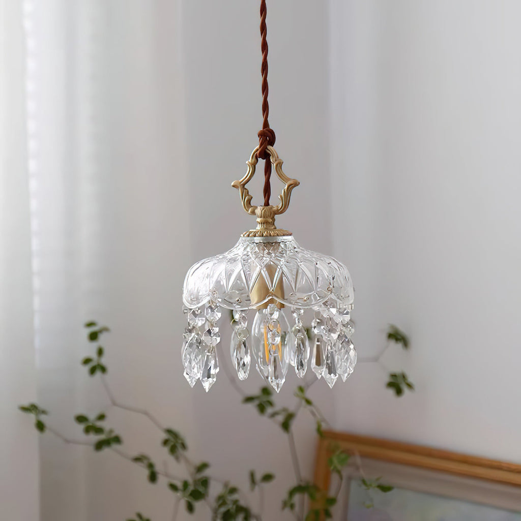 Unlit, this Clérachic pendant light shows its patterned glass dome and crystal drops, with sheer curtains and a leafy stem behind.
