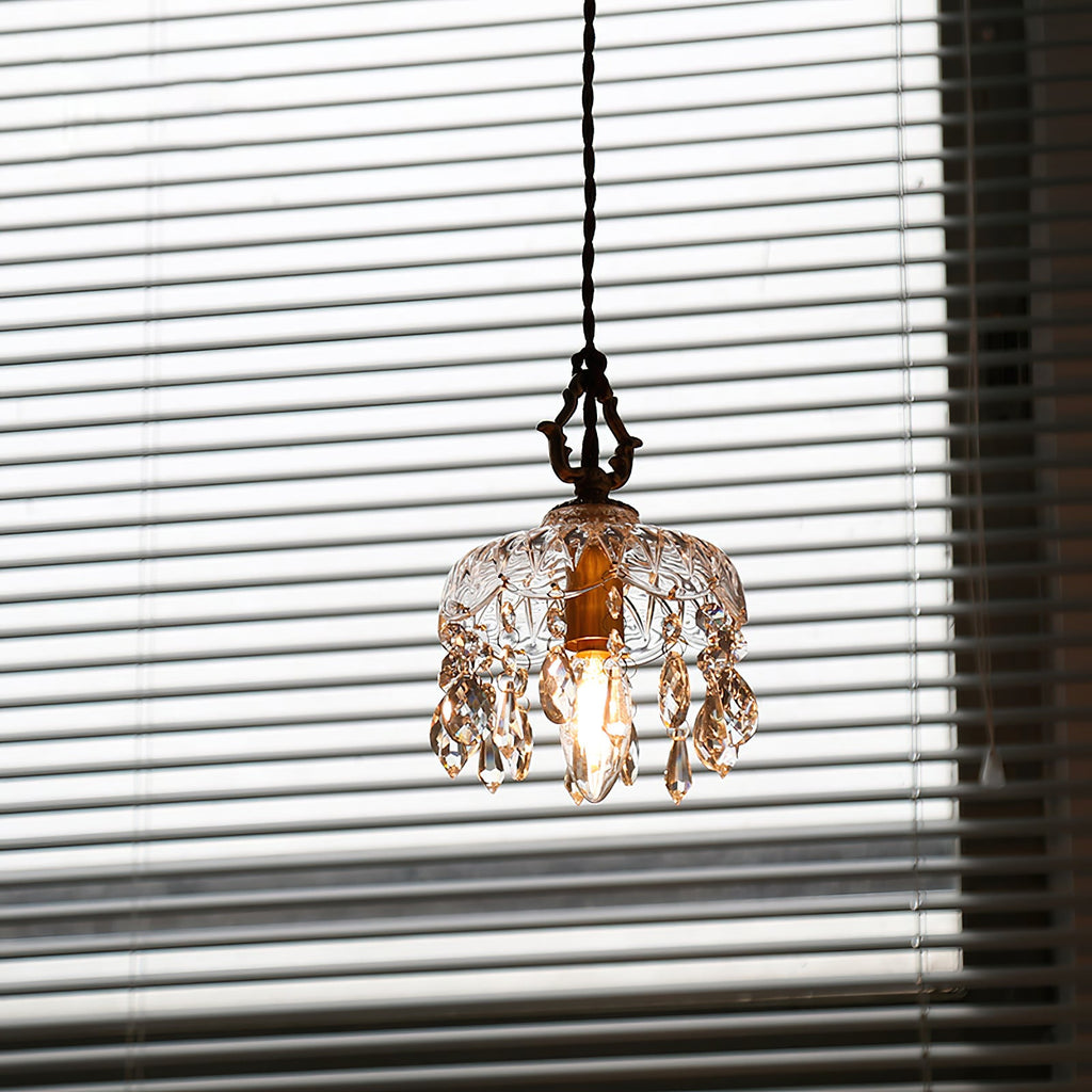 Backlit by a blinded window, this Clérachic pendant light shows a smoky tint to its glass and drops, with the bulb glowing inside.