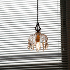 Backlit by a blinded window, this Clérachic pendant light shows a smoky tint to its glass and drops, with the bulb glowing inside.