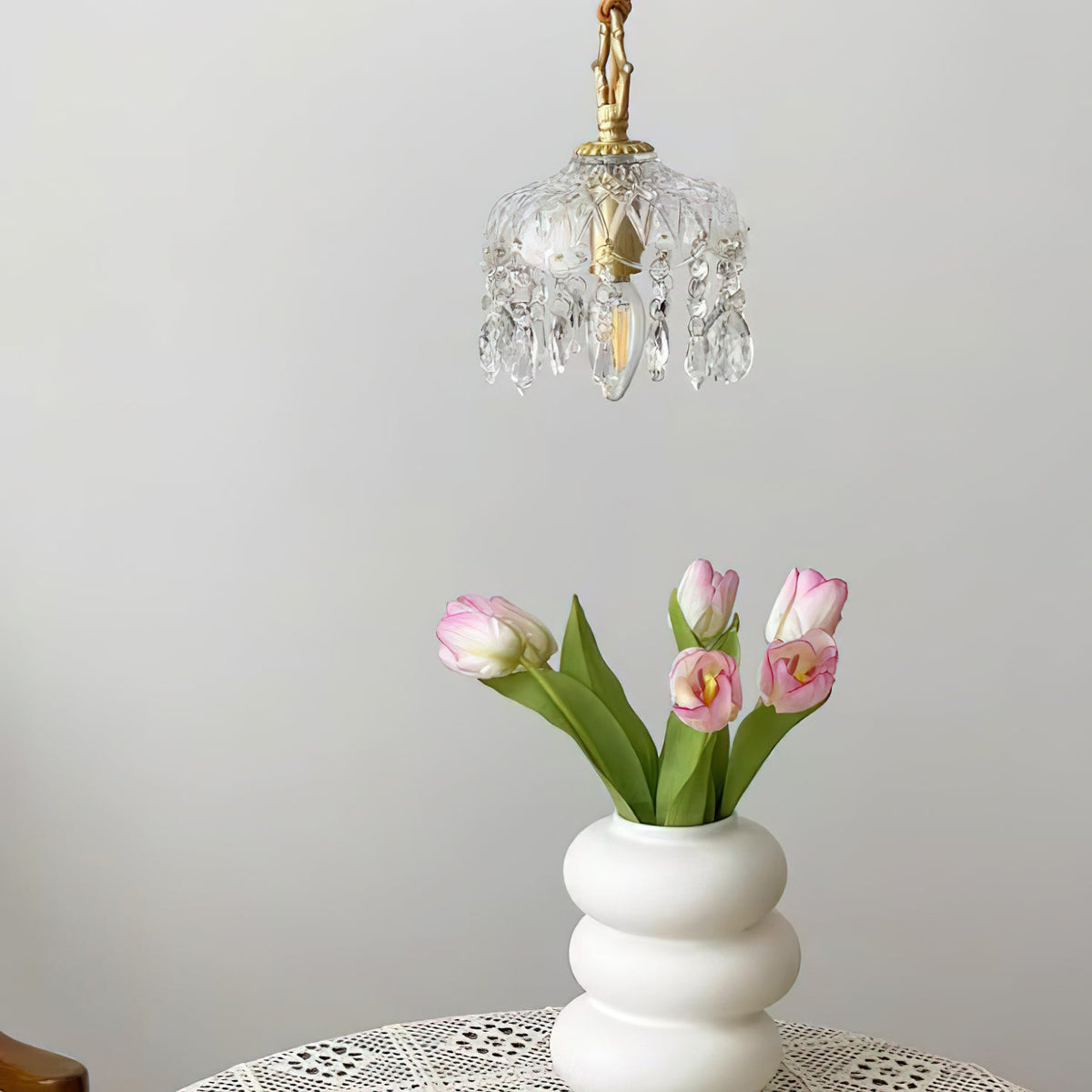 This Clérachic pendant light hangs above a white stacked vase of pink tulips on a lace-covered table.