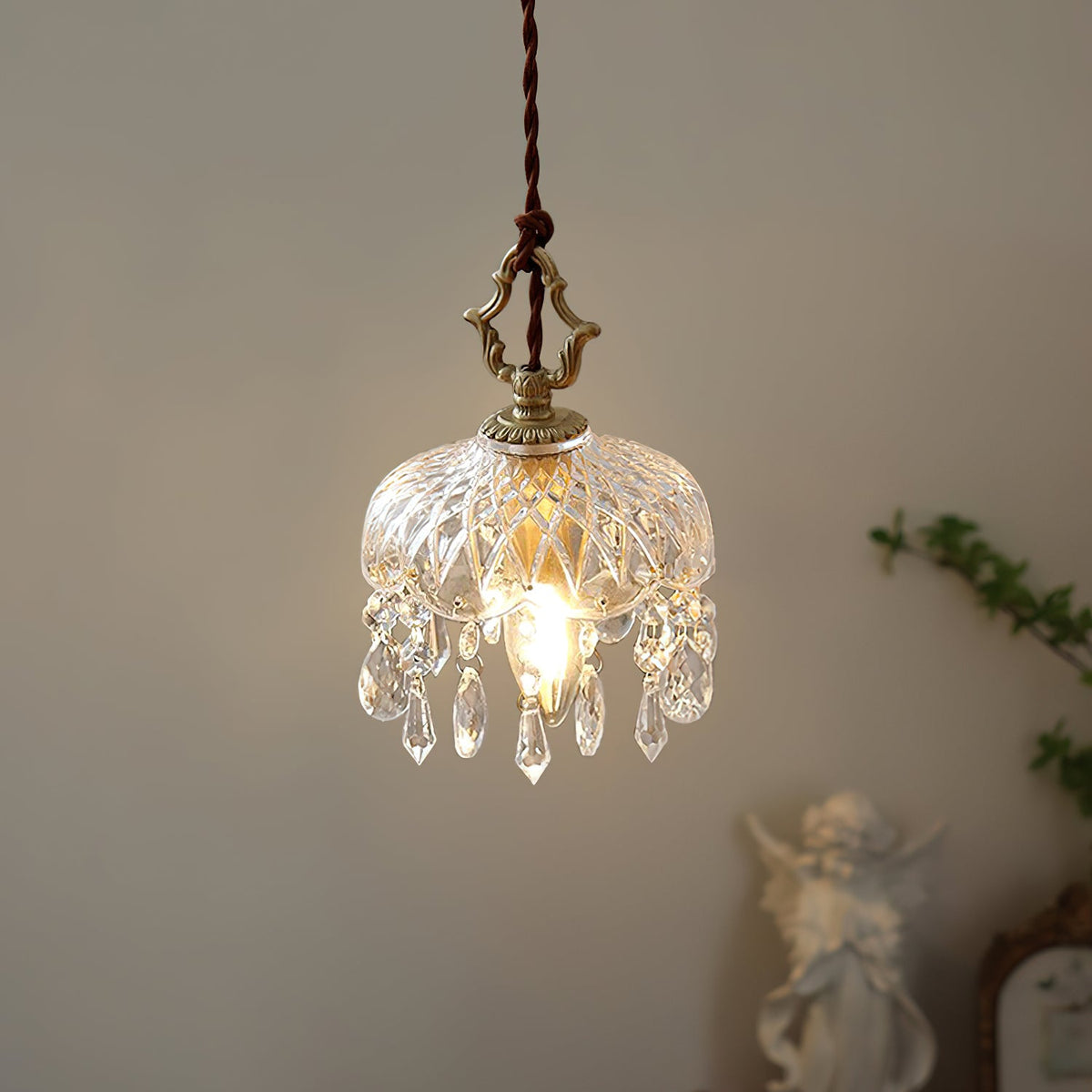 Warm and bright, this Clérachic pendant light hangs against a plain wall with a small white cherub figure in the corner.