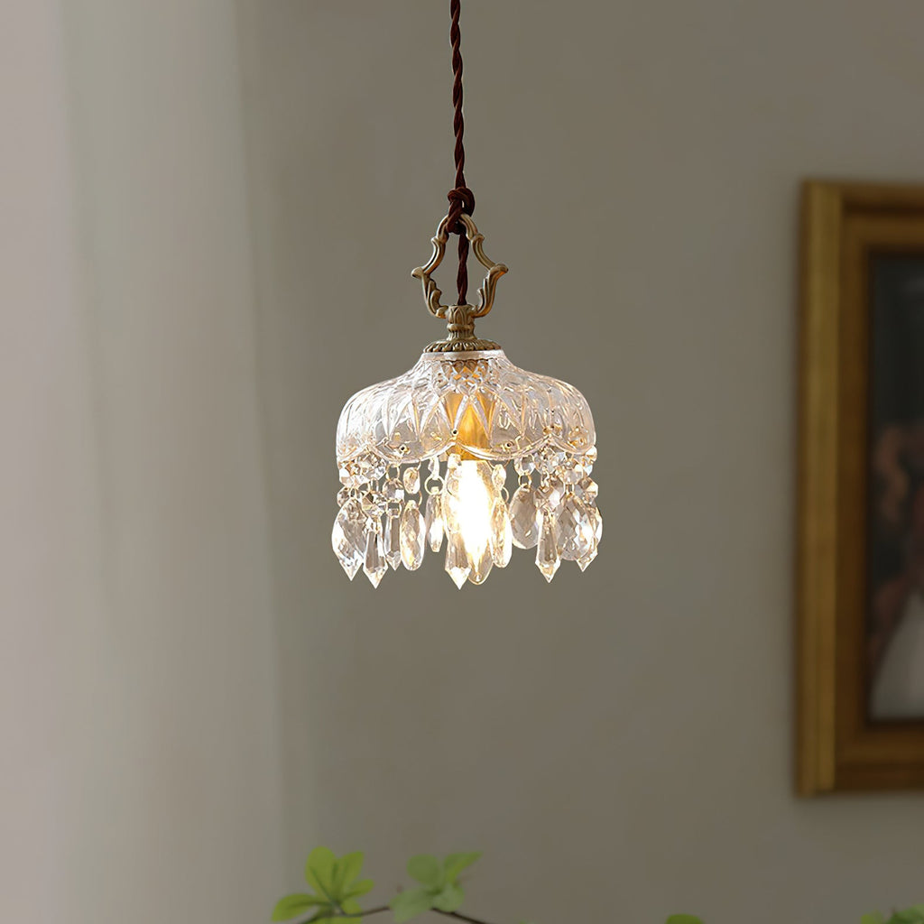 This Clérachic pendant light hangs in front of a grey wall and a gilt-framed painting, its crystal fringe lit by the bulb.