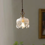 This Clérachic pendant light hangs in front of a grey wall and a gilt-framed painting, its crystal fringe lit by the bulb.
