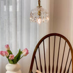 High in the frame, this Clérachic pendant light hangs by a sheer curtain, with pink tulips and a spindle-back chair below.