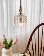Seen through sheer white curtains, this Clérachic pendant light glows above tulips and the curved back of a wooden chair.