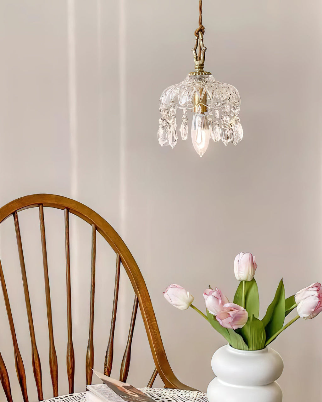 A Clérachic pendant light hangs above a spindle-back chair and a white vase of pink tulips in a soft-lit room.