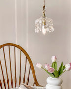 A Clérachic pendant light hangs above a spindle-back chair and a white vase of pink tulips in a soft-lit room.