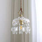 Close view of the cut-glass dome, filament bulb and teardrop crystals of this Clérachic pendant light against white curtains.
