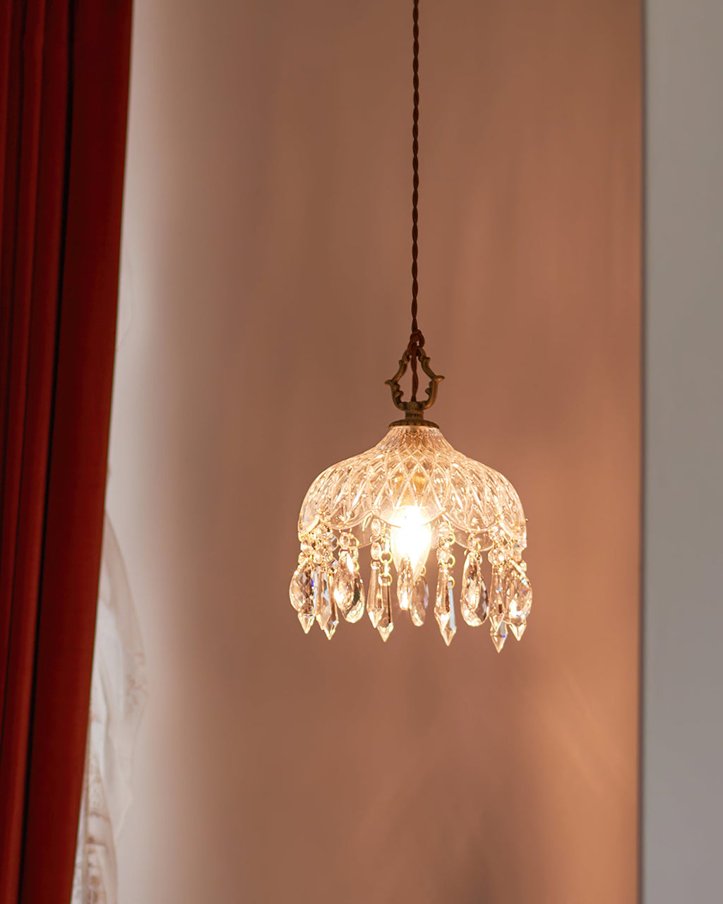 Seen from a distance, this Clérachic pendant light glows in a dusty-pink room beside a deep red curtain.