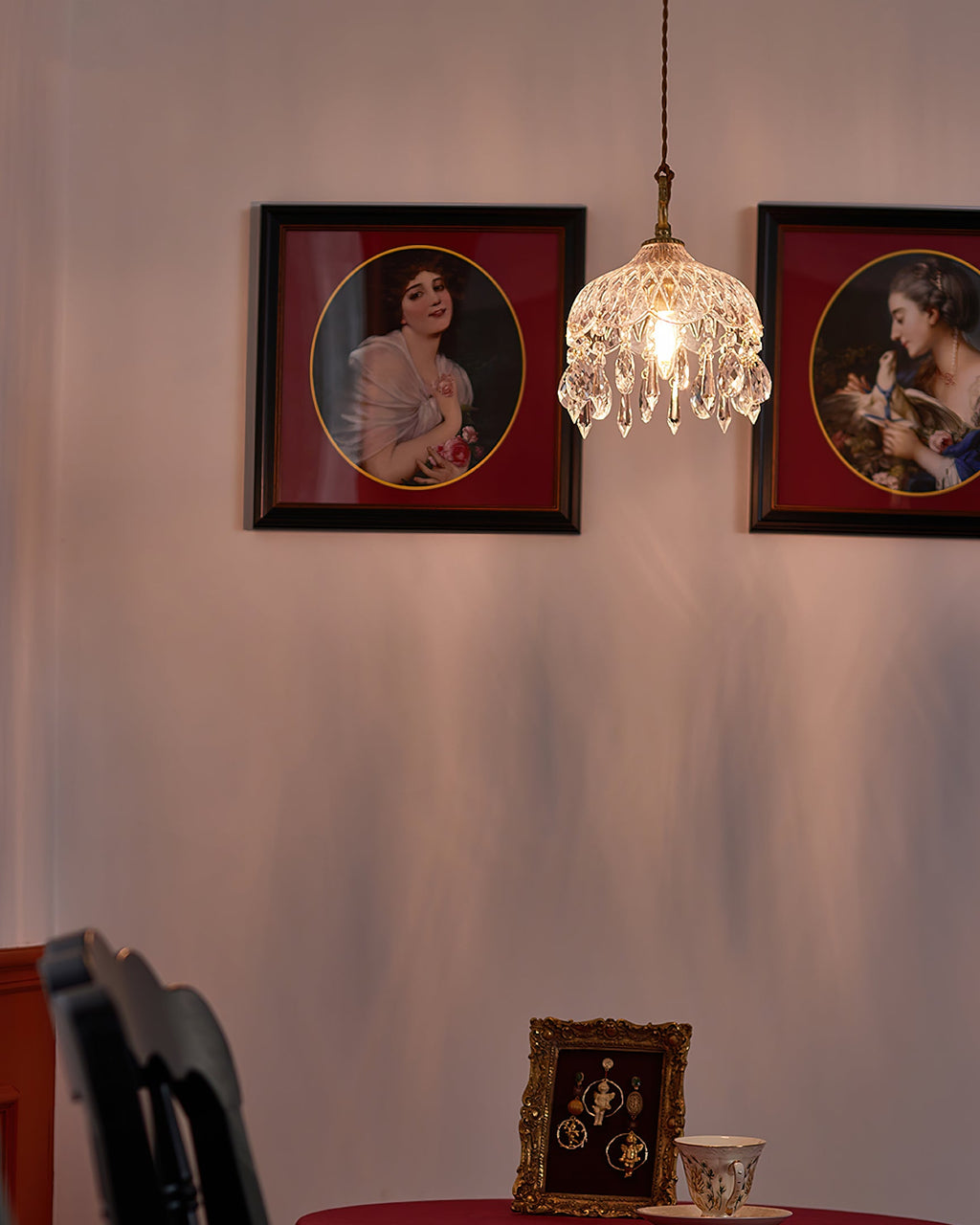 Beside two framed portraits on a rose-pink wall, this Clérachic pendant light glows over a table set with a teacup.