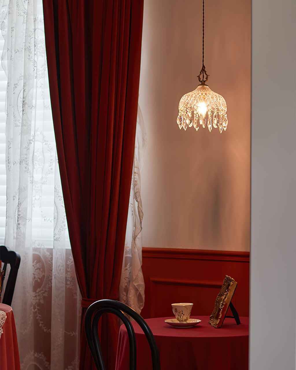 This Clérachic pendant light hangs in a window corner with a red velvet curtain and a table set with a cup and saucer.