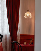 This Clérachic pendant light hangs in a window corner with a red velvet curtain and a table set with a cup and saucer.