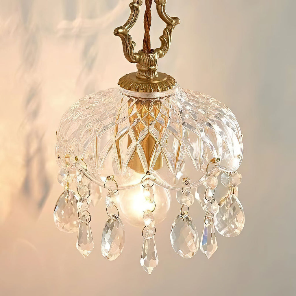 Close view of this Clérachic pendant light, with a carved gold-coloured hanger, patterned glass dome and crystal drops, glowing warmly.