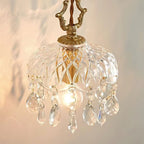 Close view of this Clérachic pendant light, with a carved gold-coloured hanger, patterned glass dome and crystal drops, glowing warmly.