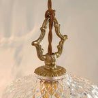 Close view of the carved brass hanger and twisted cord where this Clérachic pendant light meets its glass dome.