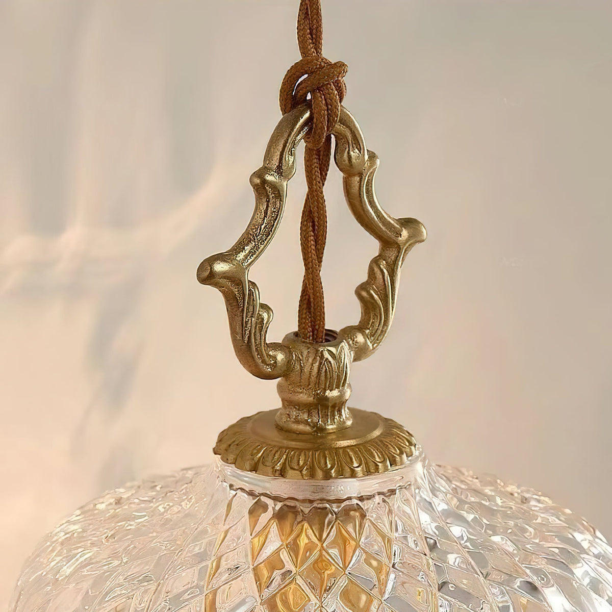 Close view of the carved brass hanger and twisted cord where this Clérachic pendant light meets its glass dome.