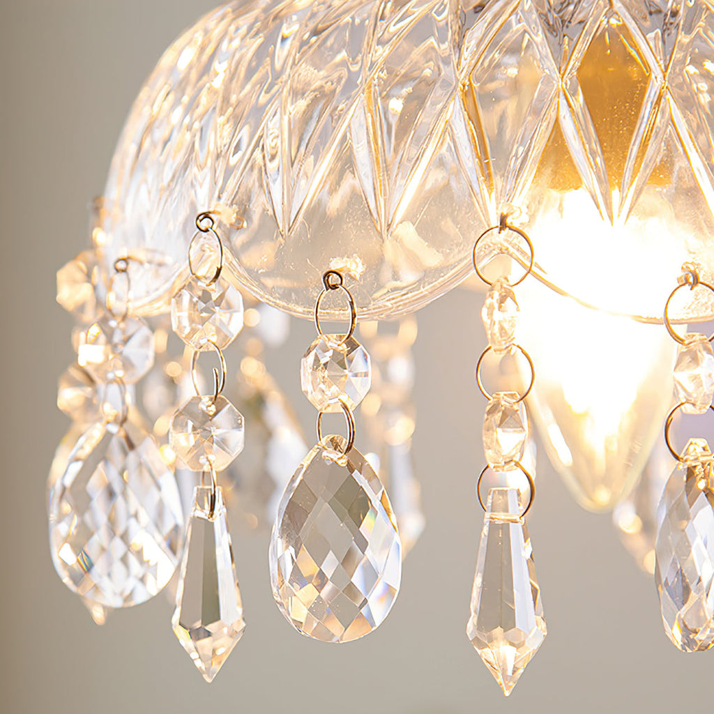 Close view of the diamond-cut glass and hanging crystal drops of this Clérachic pendant light, with the bulb glowing behind.