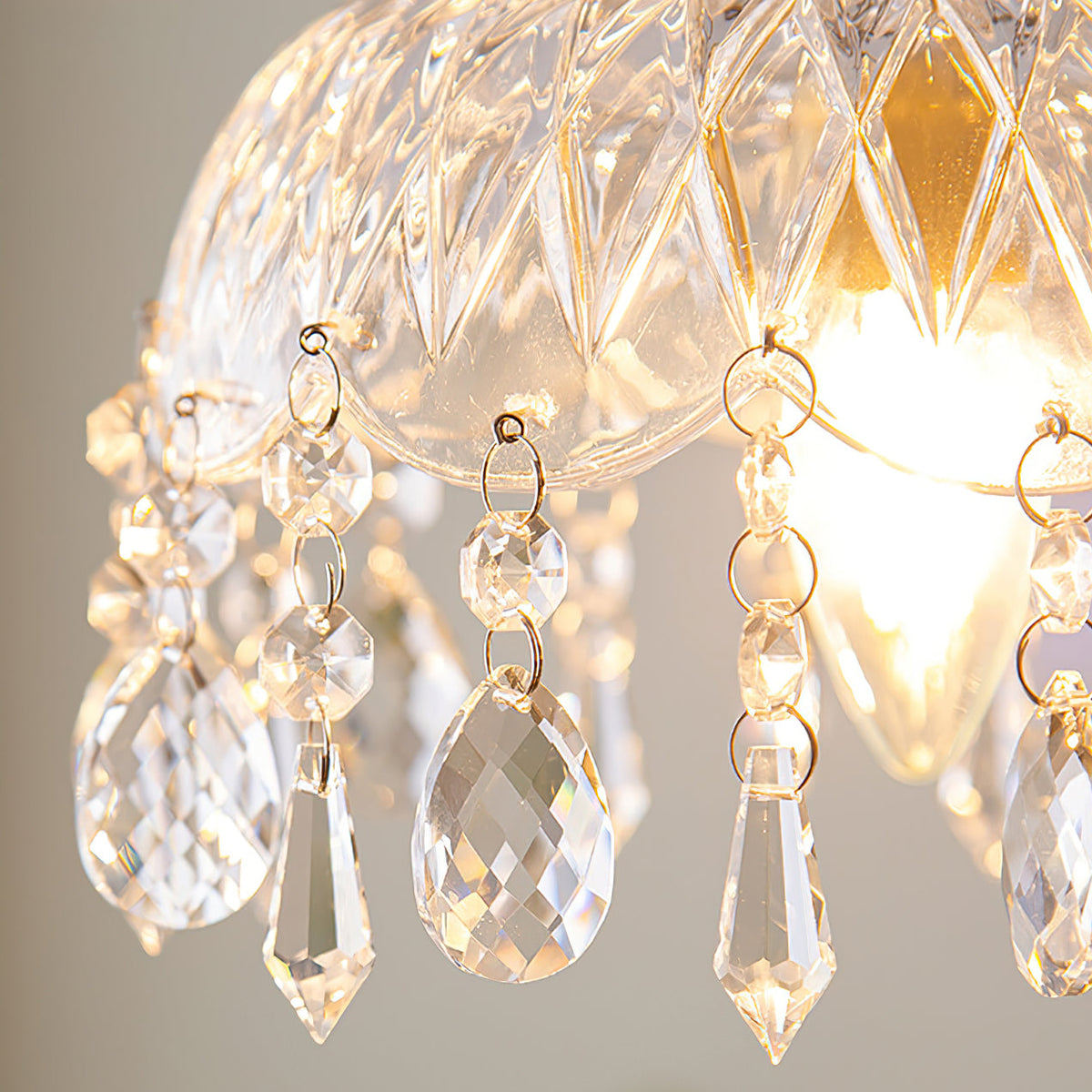 Close view of the diamond-cut glass and hanging crystal drops of this Clérachic pendant light, with the bulb glowing behind.