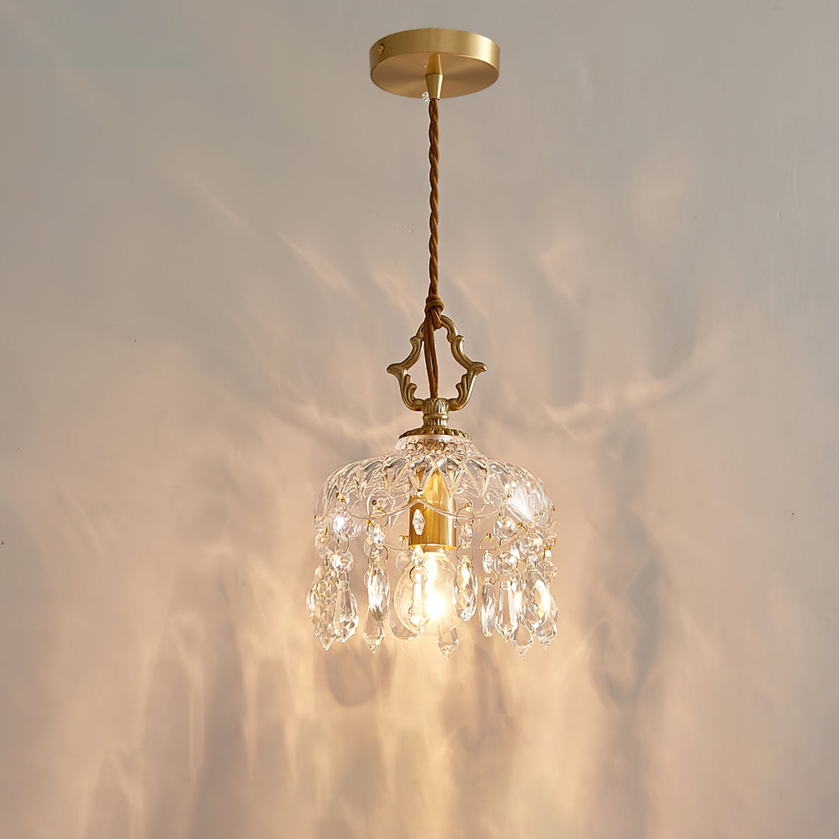 Lit against a softly rippled wall, this Clérachic pendant light hangs from a round gold ceiling plate on a twisted cord.