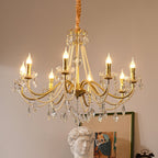 A Clérachic gold chandelier with lit candle bulbs, pearl strands and crystal drops, with a plaster bust and framed print behind.