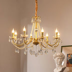 Lit candle-style bulbs on the curving gold arms of this Clérachic chandelier, with crystal drops below and a framed print at the side.