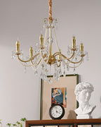 A Clérachic crystal chandelier with unlit candle-style bulbs, above a mantel with a plaster bust, a framed print and a small clock.