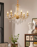 A Clérachic gold chandelier with lit candle bulbs and pearl strands, with a plaster bust and a leafy stem on a cabinet below.
