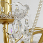 Close view of a glass candle cup, a faceted crystal drop and pearl beads on the gold arm of this Clérachic chandelier.