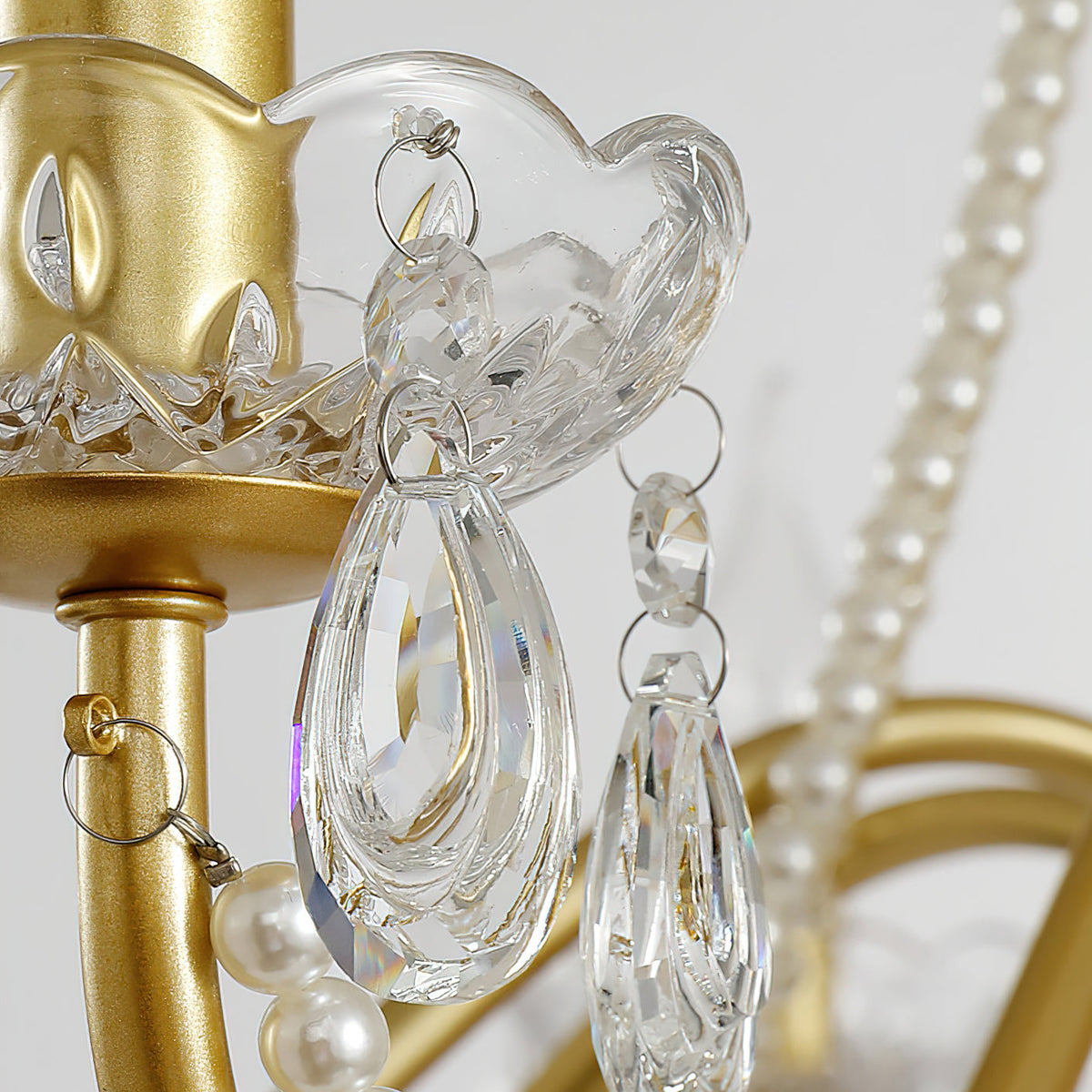 Close view of a glass candle cup, a faceted crystal drop and pearl beads on the gold arm of this Clérachic chandelier.