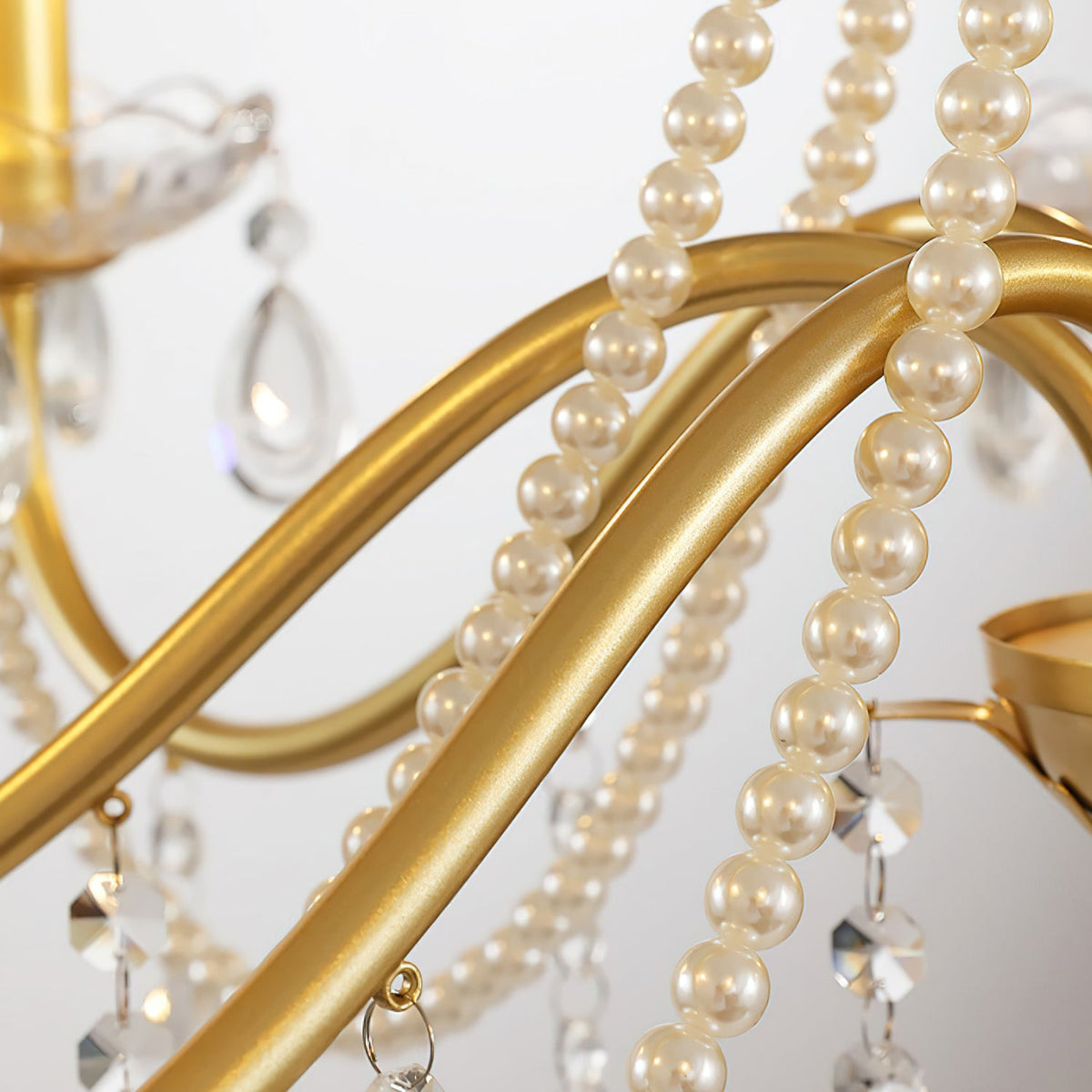 Close view of the curving gold arms of this Clérachic chandelier, wrapped with pearl strands and hung with crystal drops.