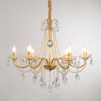 A Clérachic gold chandelier with lit candle-style bulbs, crystal drops and pearl strands on a soft grey backdrop.