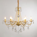 A Clérachic gold crystal chandelier with lit flame-tip bulbs and pearl strands, hung on a wrapped chain against a grey backdrop.