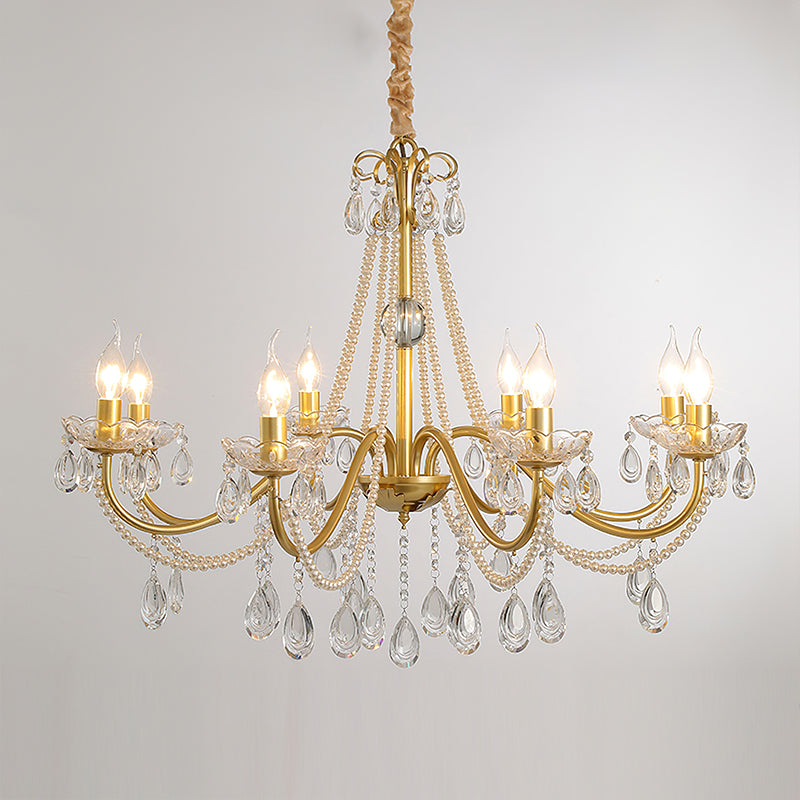A wide Clérachic gold chandelier with lit candle bulbs and many crystal drops, hung on a wrapped chain against a pale grey backdrop.