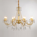 A wide Clérachic gold chandelier with lit candle bulbs and many crystal drops, hung on a wrapped chain against a pale grey backdrop.