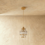 Clérachic three-tier crystal pendant on a gold cord and canopy, unlit, hung against a soft plaster wall.