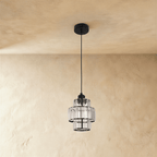 Clérachic three-tier crystal pendant on a black cord and canopy, unlit, against a pale plaster wall.