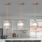 Three Clérachic gold-framed crystal pendants hung in a row above a white kitchen island with cabinets behind.