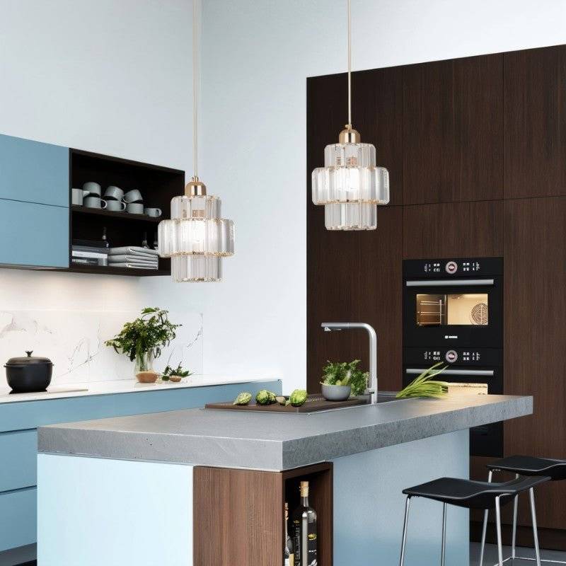 Two Clérachic gold crystal pendants over a kitchen island with blue cabinets and a dark wood oven wall.