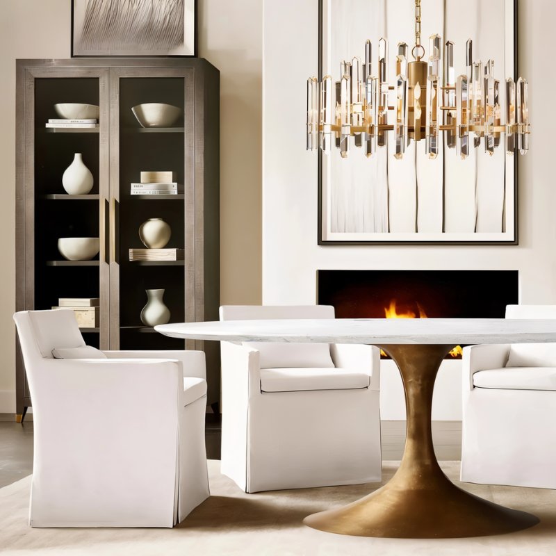 Clérachic round chandelier of clear crystal rods with brass arms hanging above an oval marble dining table and white chairs.