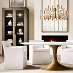 Clérachic round chandelier of clear crystal rods with brass arms hanging above an oval marble dining table and white chairs.