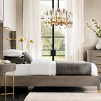 Clérachic small brass and crystal-rod chandelier hanging in a bedroom by a tall window, above a low grey bed.