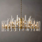 Clérachic widest round chandelier of clear crystal rods on a brass frame, with many candle bulbs, on a grey ground.